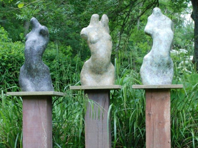 set of three abstract human forms in polished stone set on tall timber plinths in garden